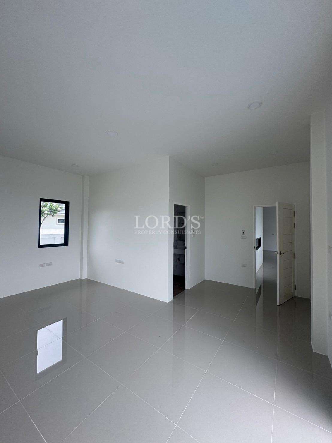 Spacious empty bedroom with tiled floor, white walls, and ensuite access