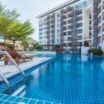 Large outdoor swimming pool at a modern condominium complex with sun loungers and landscaped surroundings.