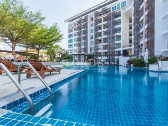 Large outdoor swimming pool at a modern condominium complex with sun loungers and landscaped surroundings.