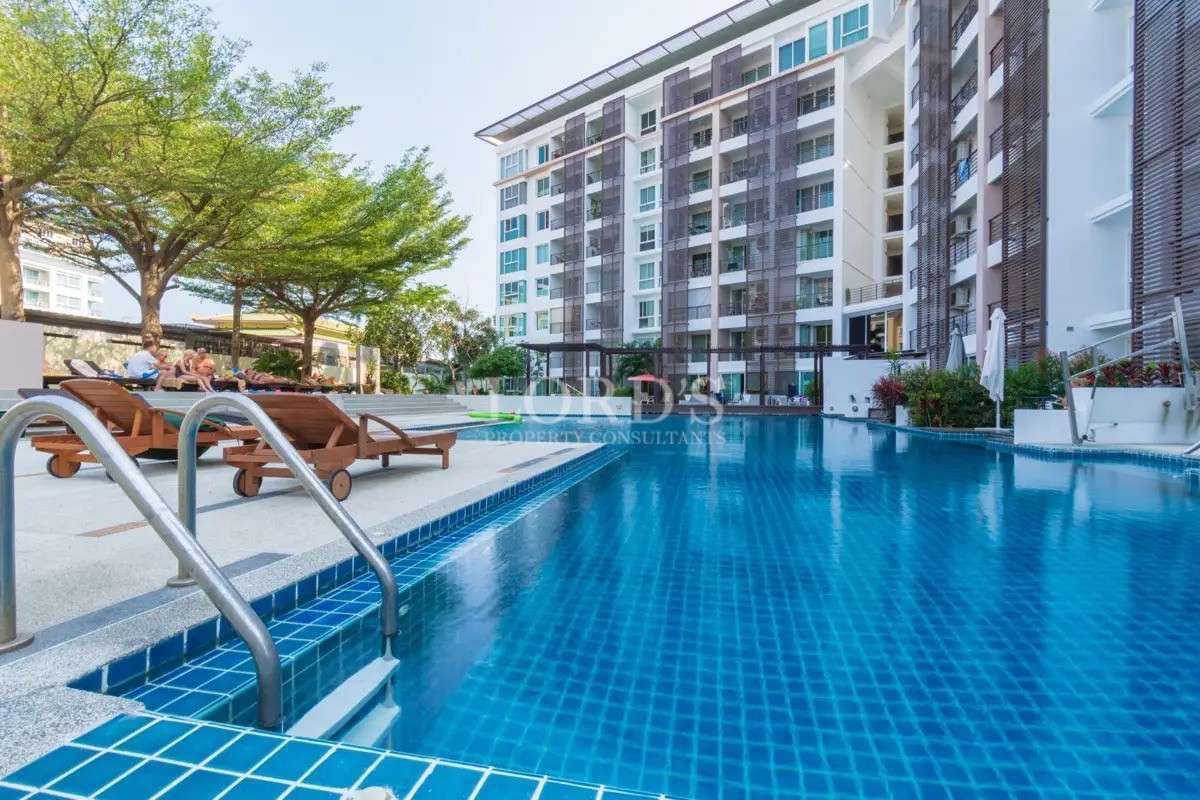 Large outdoor swimming pool at a modern condominium complex with sun loungers and landscaped surroundings.