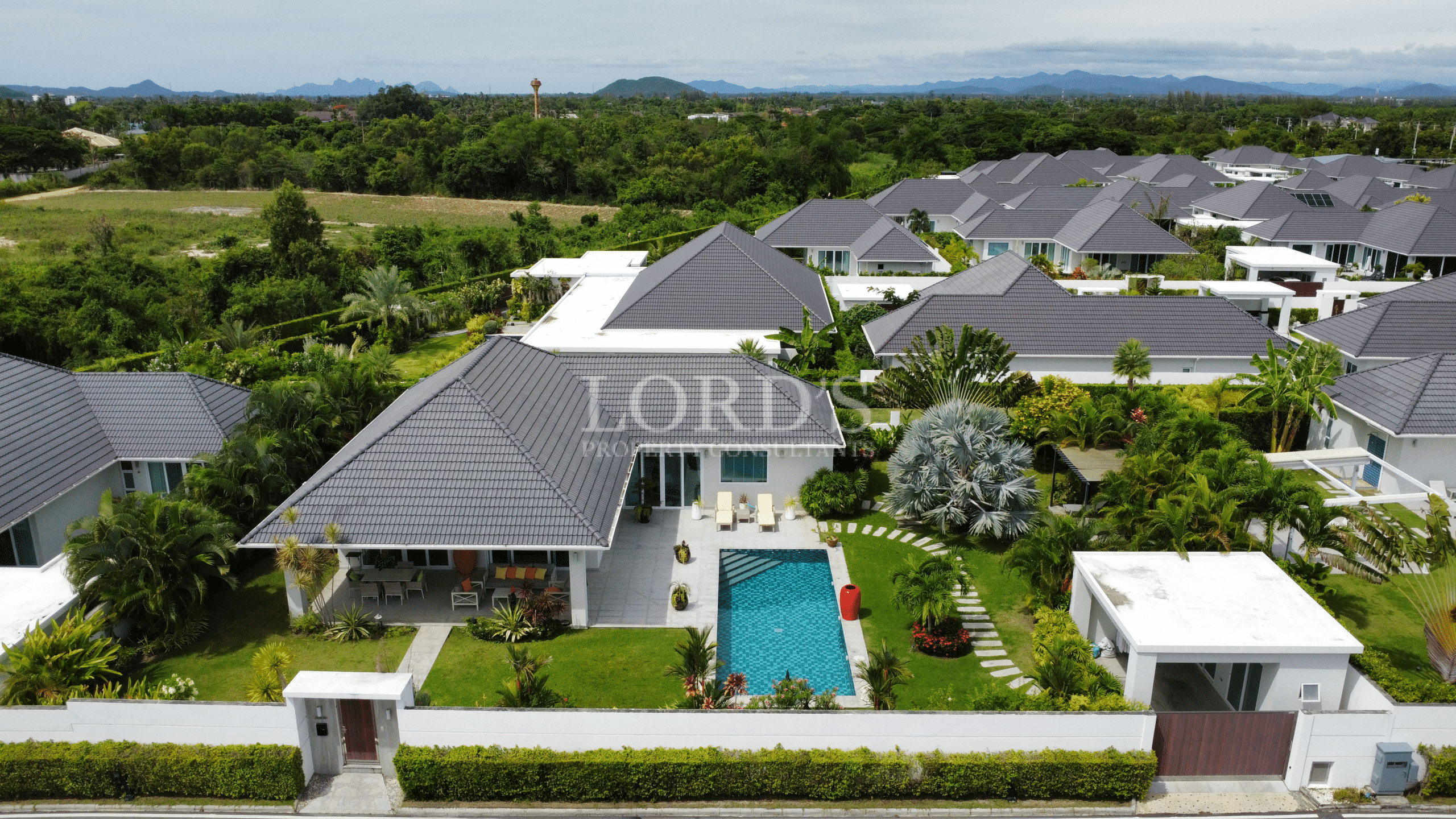 Aerial view of a modern luxury pool villa with a private swimming pool, landscaped garden, and tiled roof in a gated community.