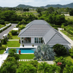 Aerial view of a modern villa with a private swimming pool, green lawn, and mountain views in a quiet residential neighborhood.