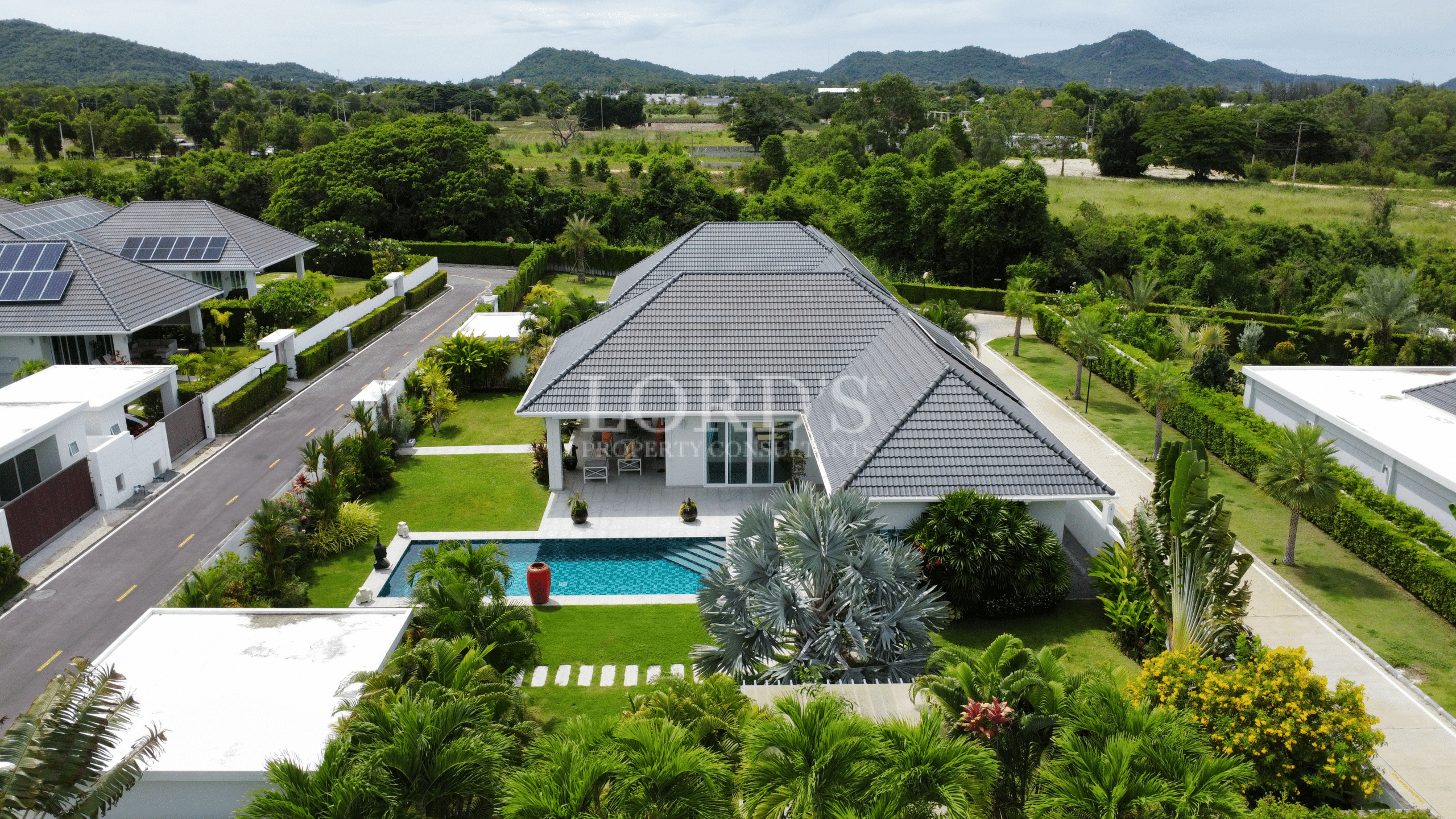 Kopie von 917 Aerial view of a modern villa with a private swimming pool, green lawn, and mountain views in a quiet residential neighborhood.