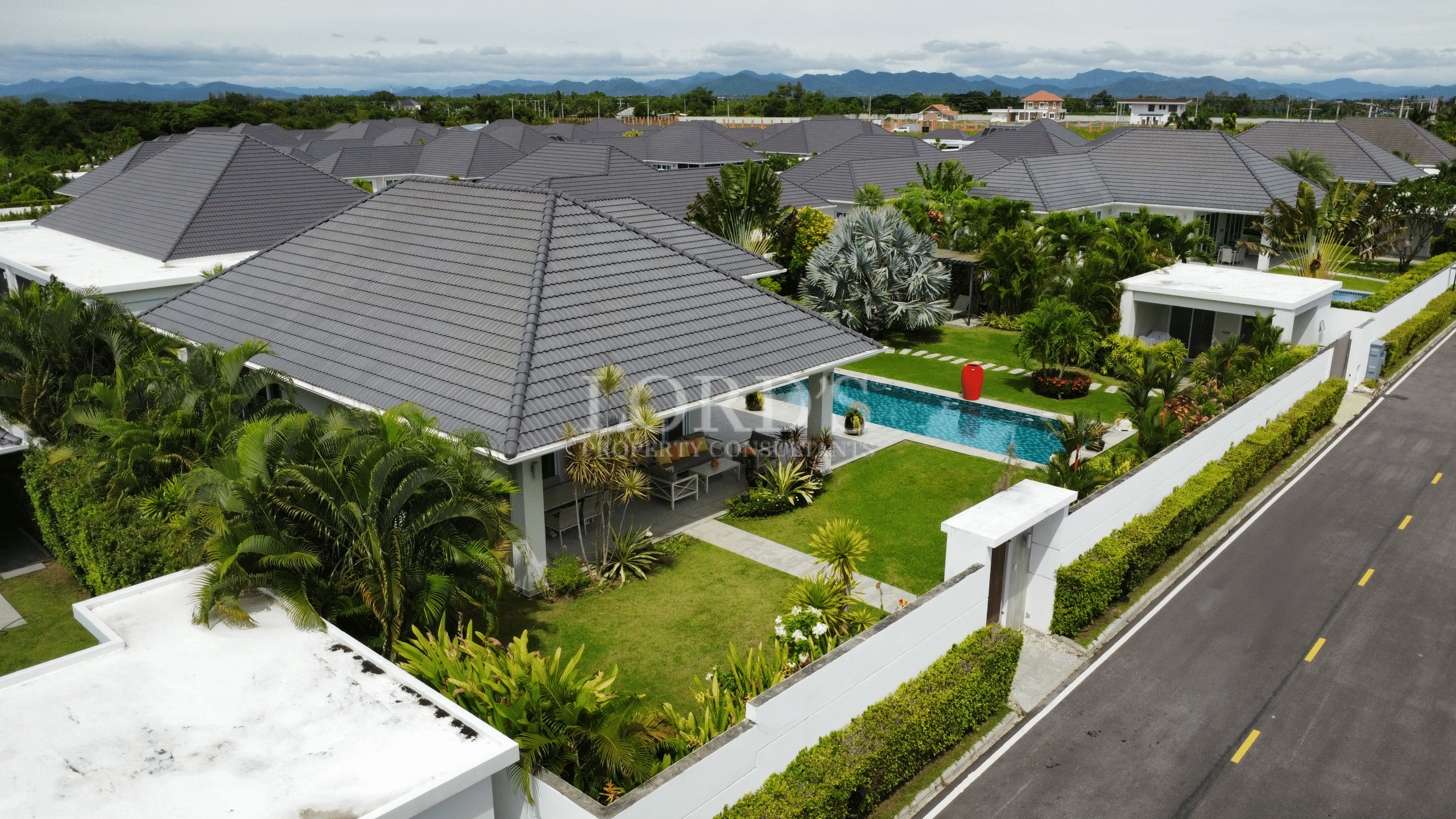 Aerial view of a modern single-story villa with a private swimming pool, landscaped garden, and tiled roof in a gated residential community.