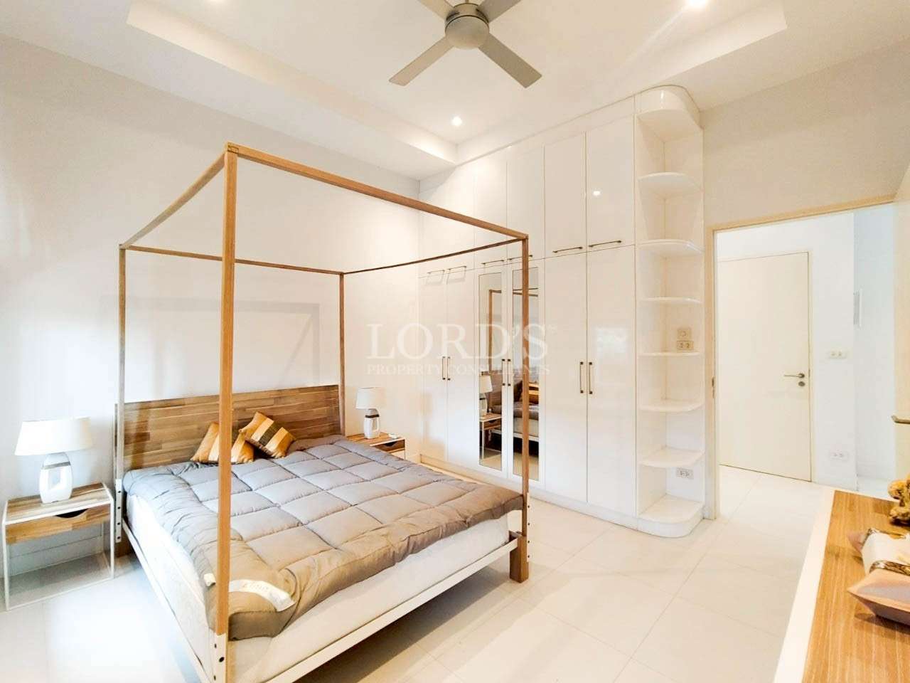 Modern minimalist bedroom with wooden four-poster bed, white built-in wardrobe, and ceiling fan