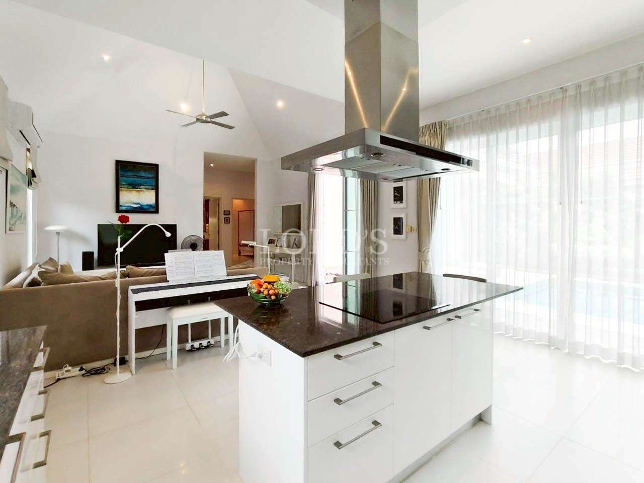 Open-plan kitchen with white cabinets, black island countertop, and stainless steel range hood