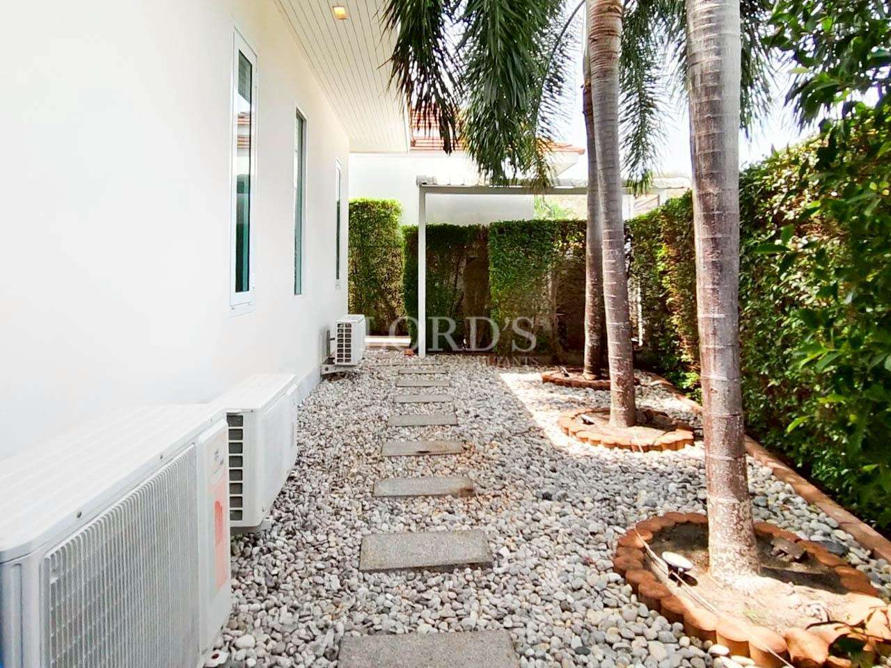 Outdoor air conditioning units installed along the side yard of a modern home with gravel pathway and palm trees