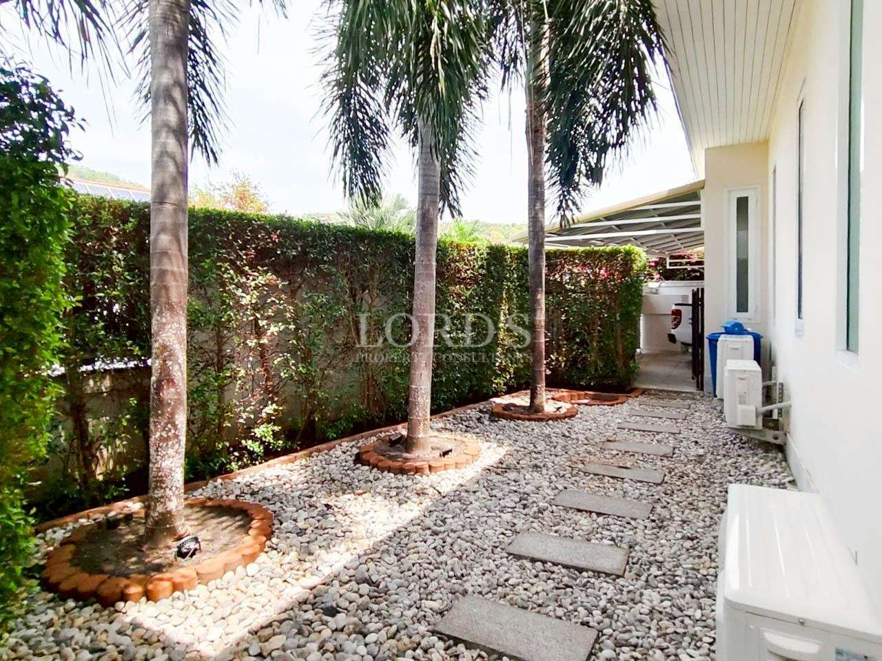Side garden walkway with palm trees, stone path, and gravel landscaping beside a villa.