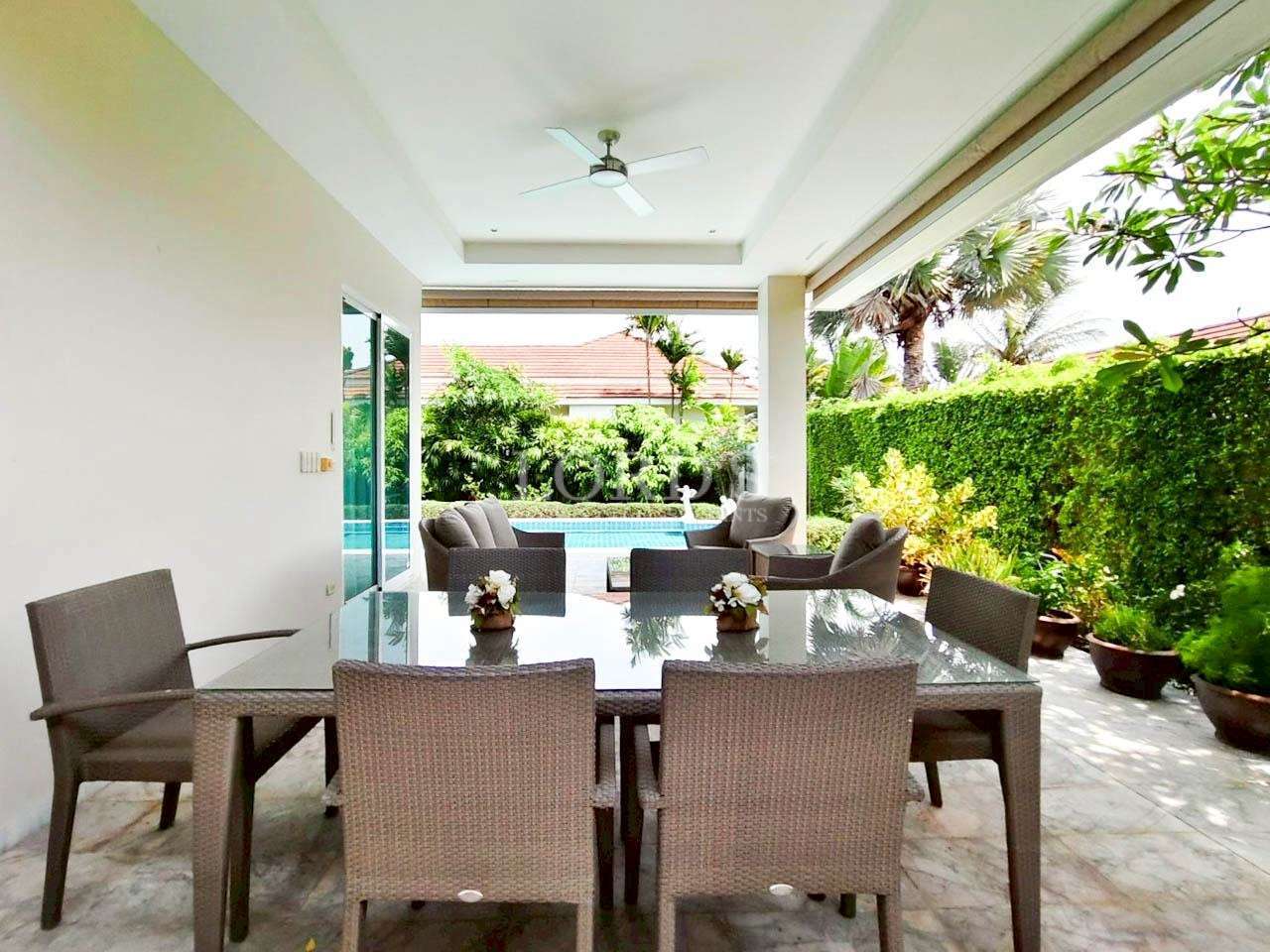 Covered villa patio with glass dining table, wicker chairs, and view of the private pool.