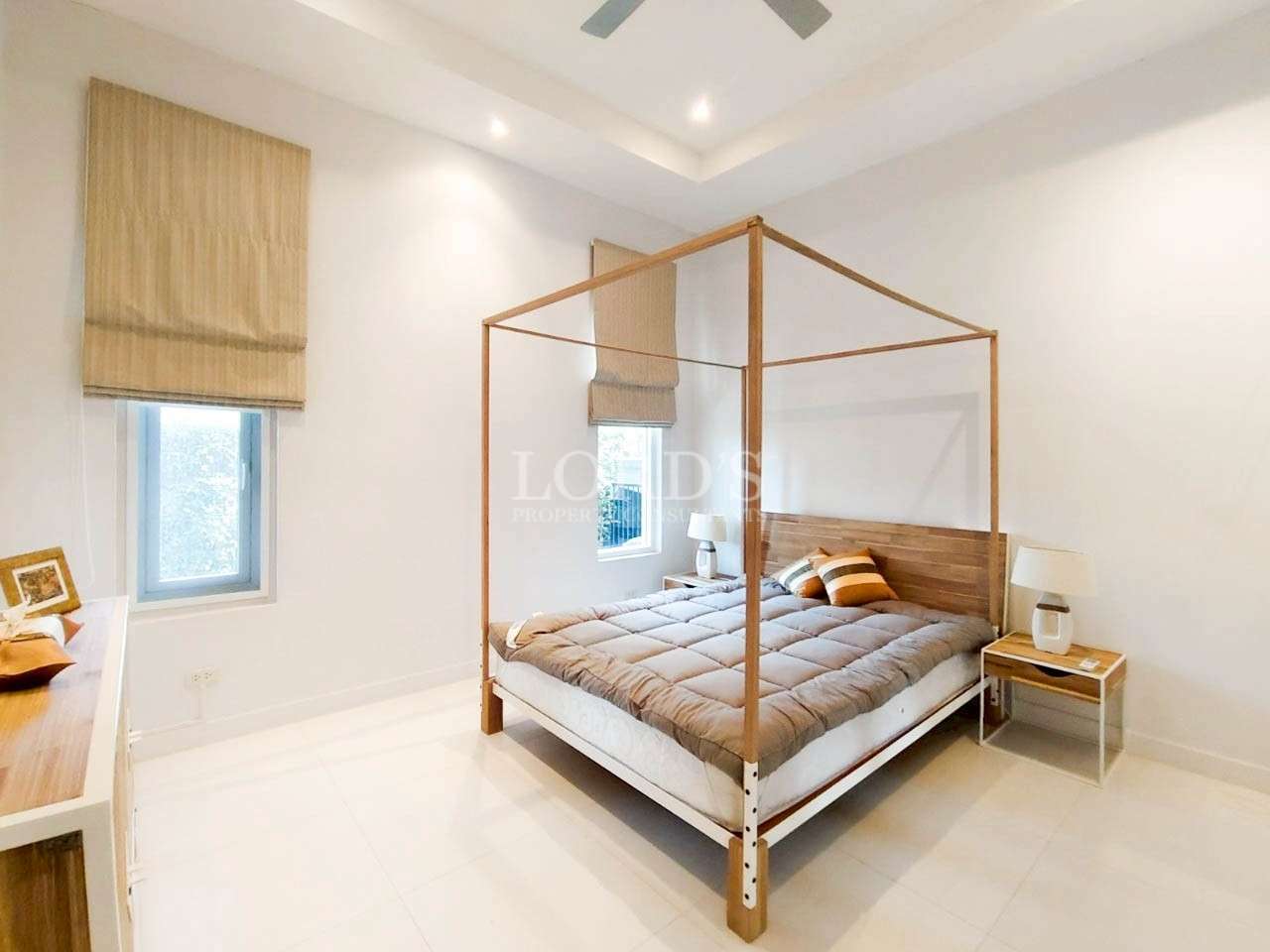 Bright minimalist bedroom with wooden four-poster bed, white walls, and soft natural light