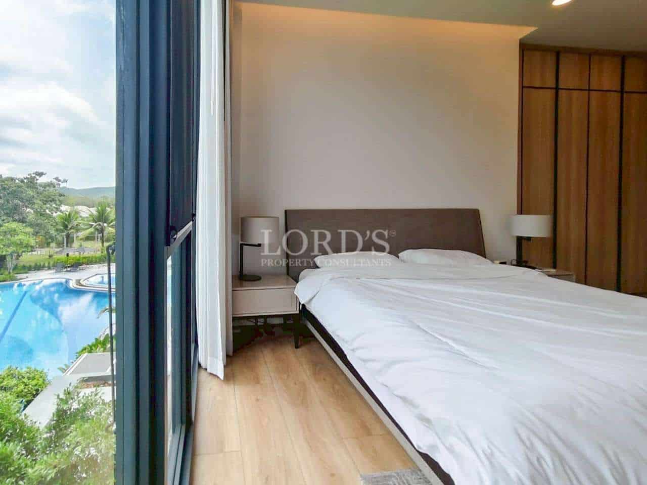 Modern bedroom with large bed and balcony view overlooking a swimming pool.