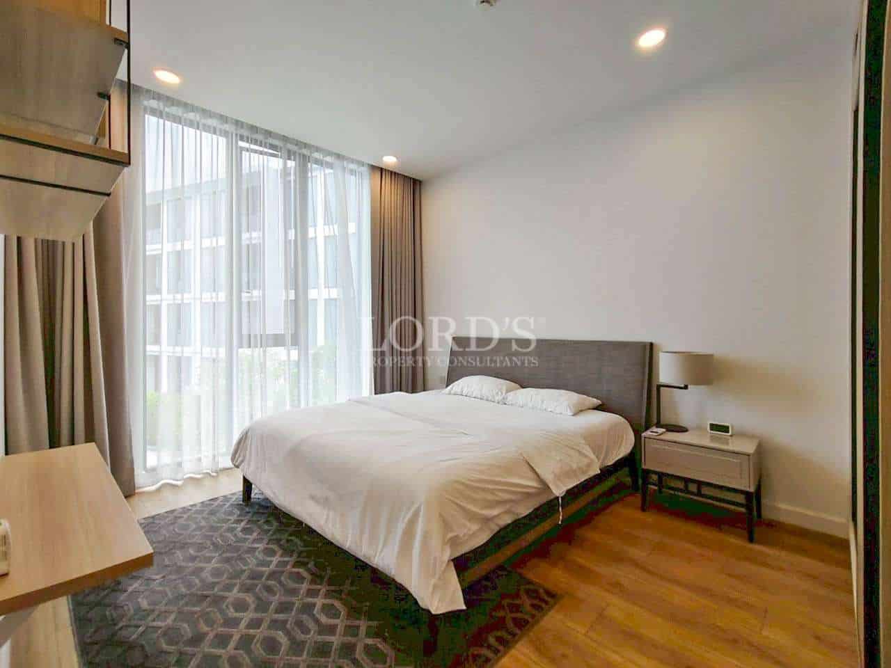 Modern bedroom with double bed, bedside table, and large window with sheer curtains.