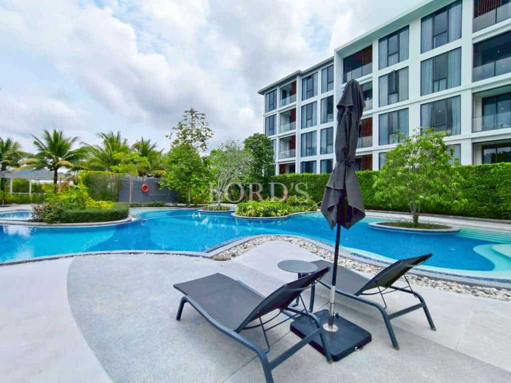 Modern condominium swimming pool with sun loungers and landscaped gardens.