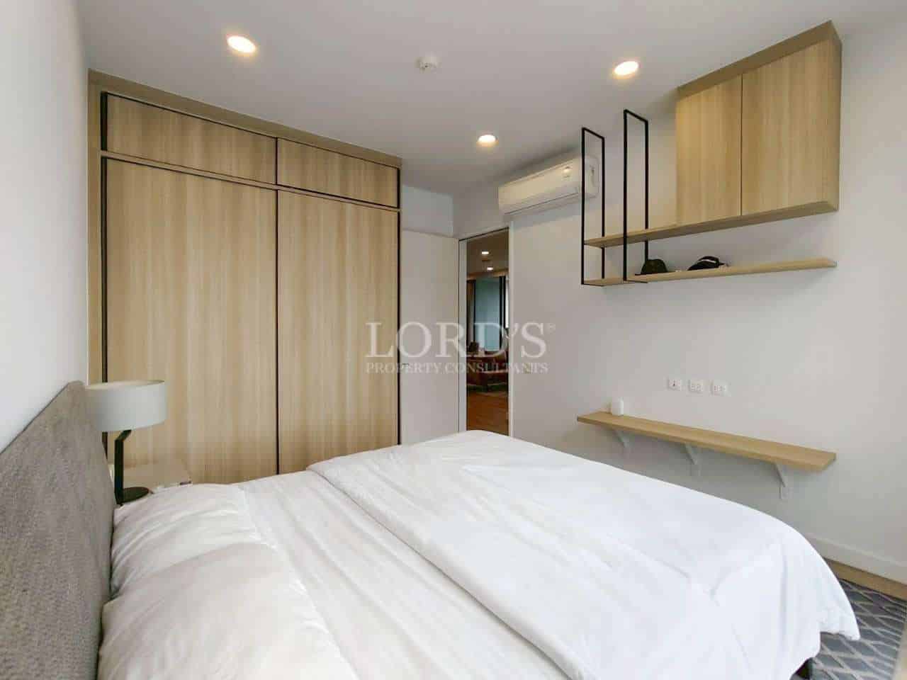 Modern bedroom with double bed, wooden wardrobe, and wall-mounted shelves.