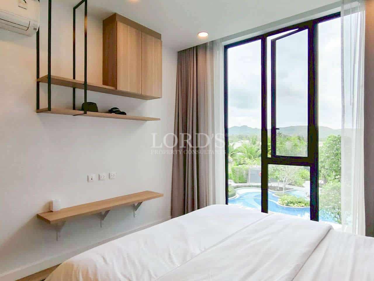 Modern bedroom with white bedding, wall shelves, and large window overlooking a pool.