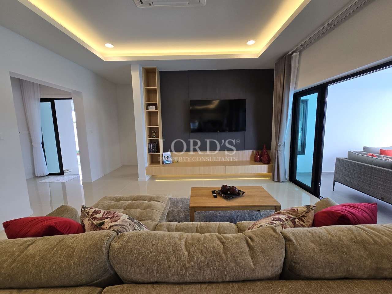 Modern living room with sofa seating, wall-mounted TV unit, and sliding glass doors.