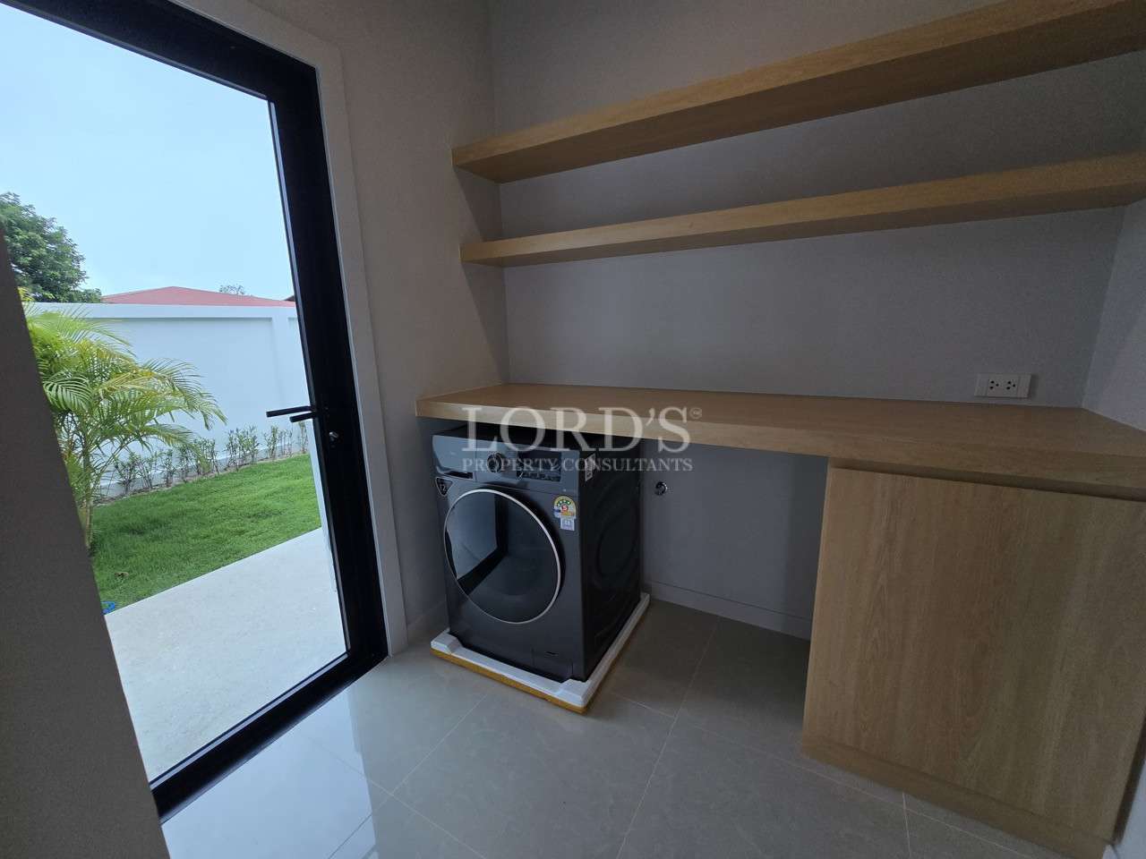 Utility room with washing machine, wooden shelves, work counter, and garden access.
