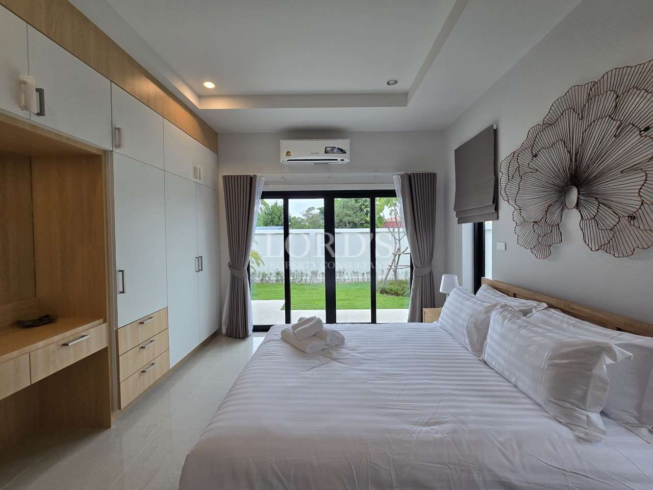 Modern bedroom with built-in wardrobe, large bed, sliding glass doors, and garden view.