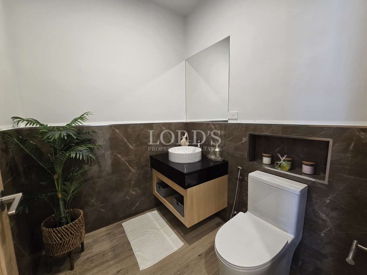 Modern guest bathroom with floating vanity, vessel sink, toilet, and decorative shelf.