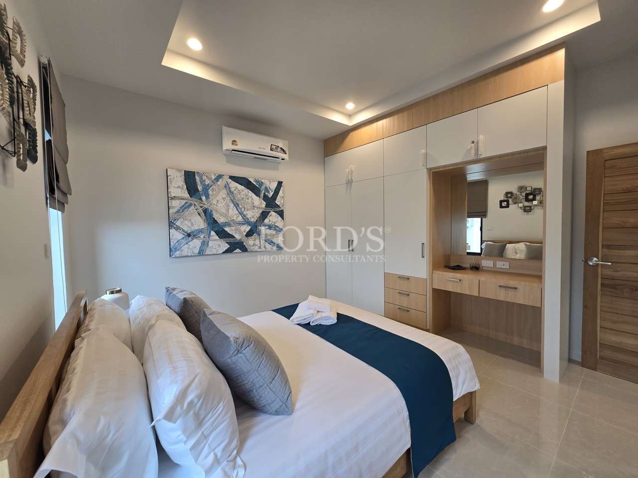 Modern bedroom with wooden bed, built-in wardrobe, vanity area, and air conditioner.