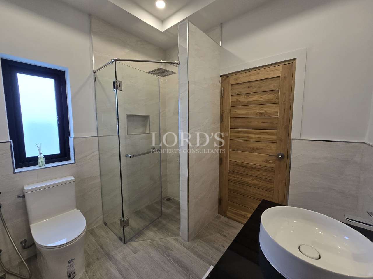 Modern bathroom with glass shower, wooden door, toilet, and vessel sink.