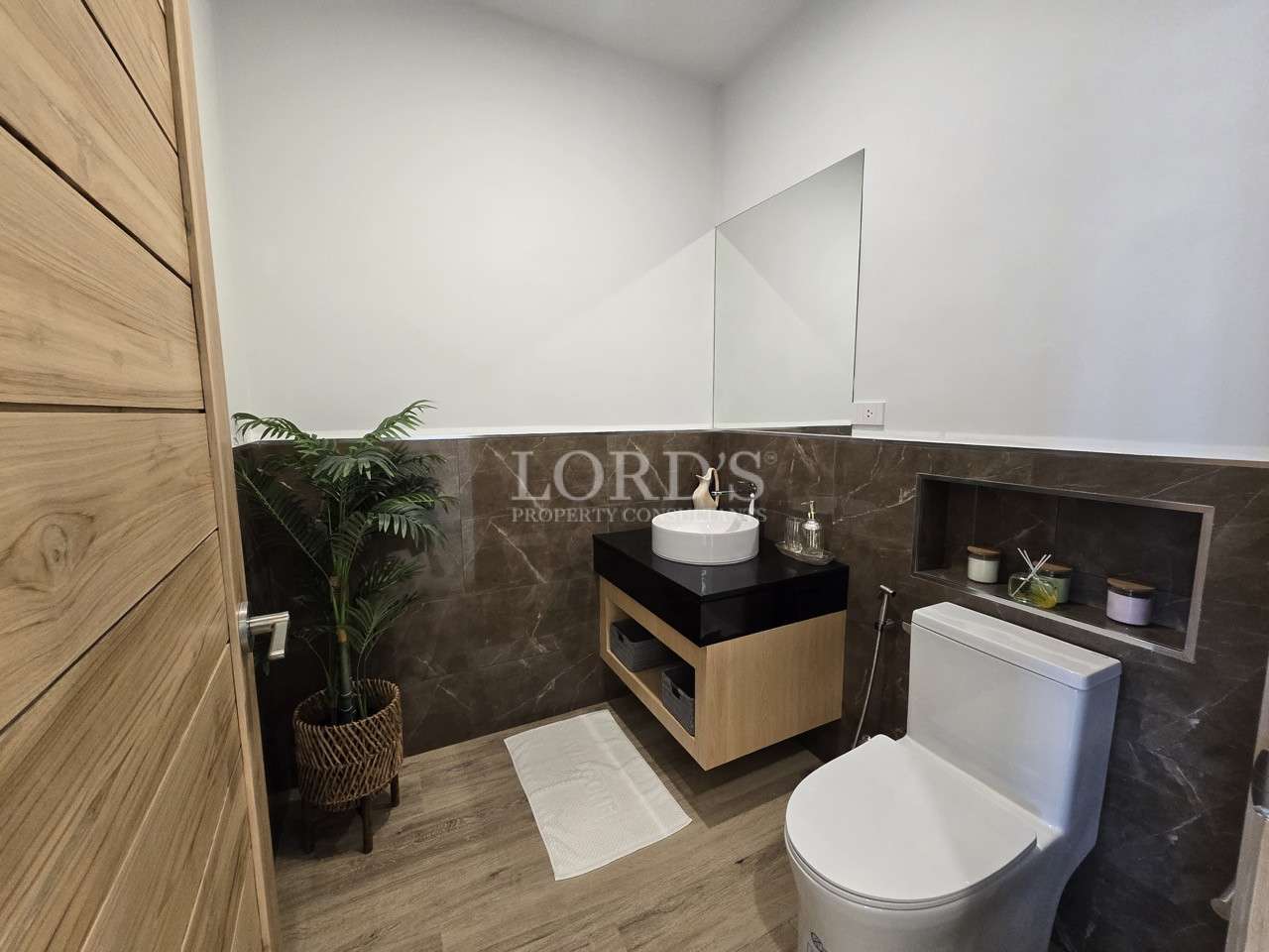 Modern guest bathroom with vanity sink, toilet, mirror, and wood accents.