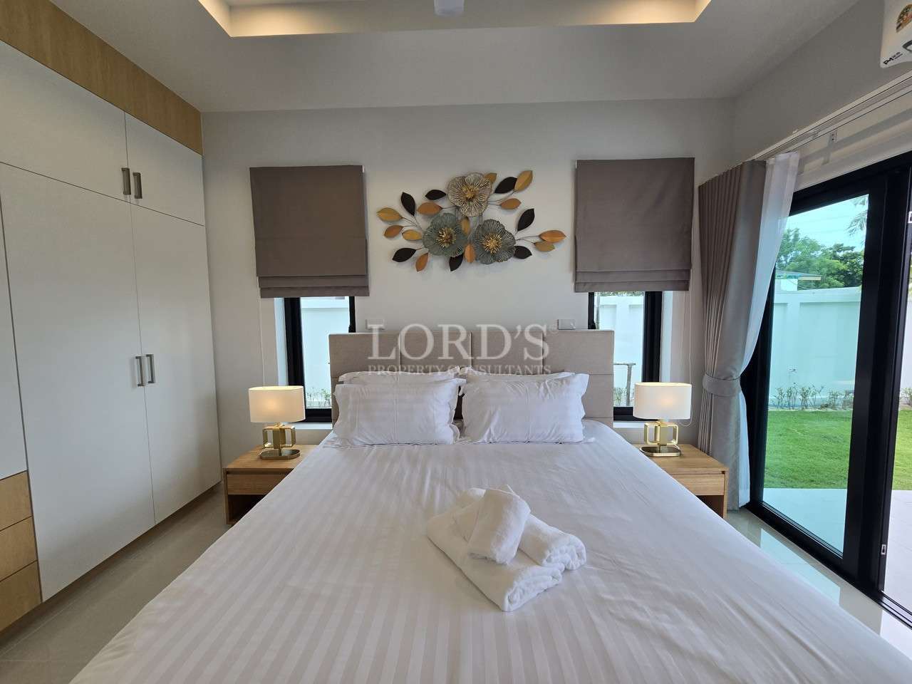 Modern bedroom with king-size bed, bedside lamps, wall art, and garden view.