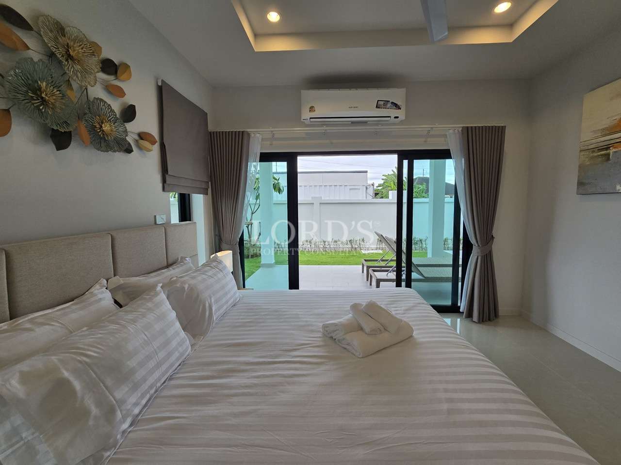Modern bedroom with large bed, air conditioner, and sliding glass doors to poolside terrace.