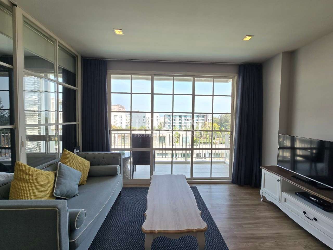 Cozy living room with sofa, coffee table, TV unit, and large sliding glass doors opening to a balcony.