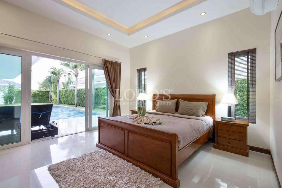 Bright bedroom with wooden bed, bedside table, and sliding doors opening to pool area.