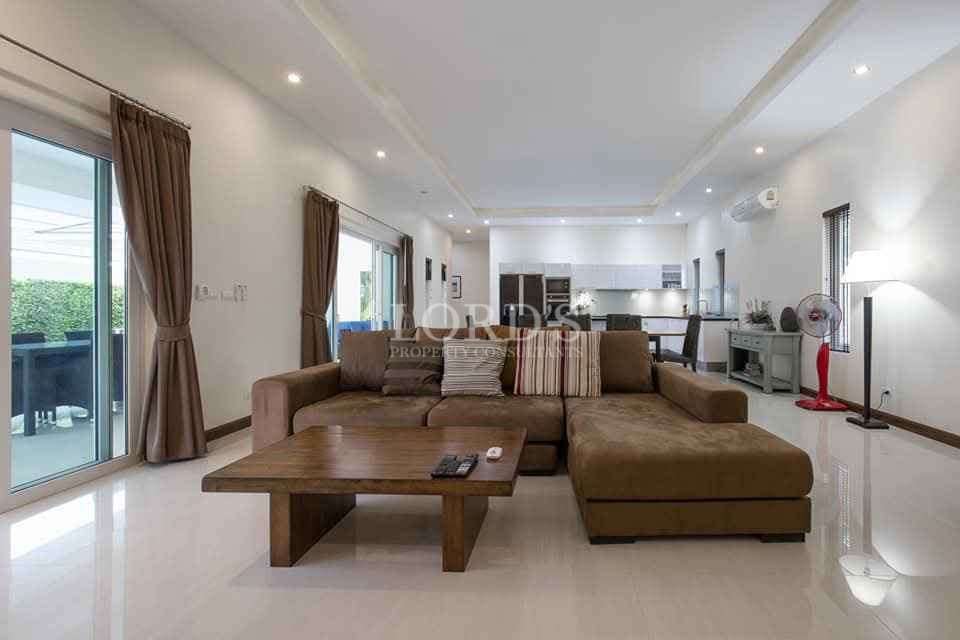 Open-plan living room with large sectional sofa, coffee table, and modern kitchen in background.