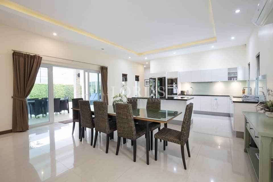 Open-plan dining area with glass table, modern kitchen, and sliding doors to outdoor patio.