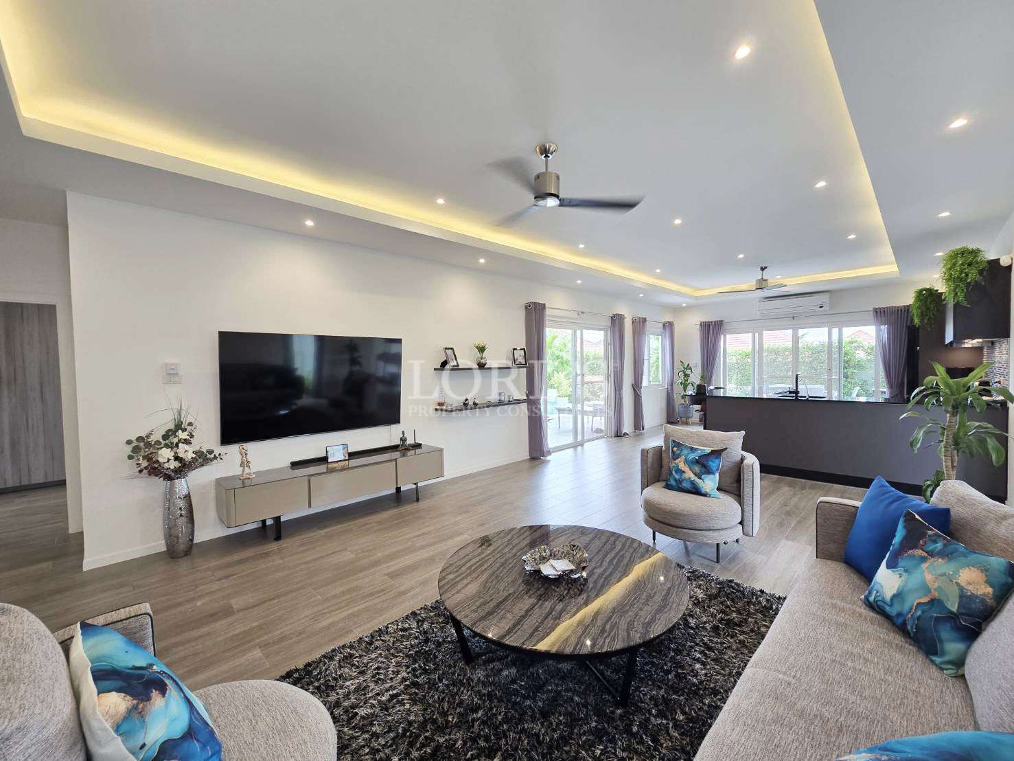 Modern open-plan living room with wall-mounted TV, sofa seating, and contemporary lighting