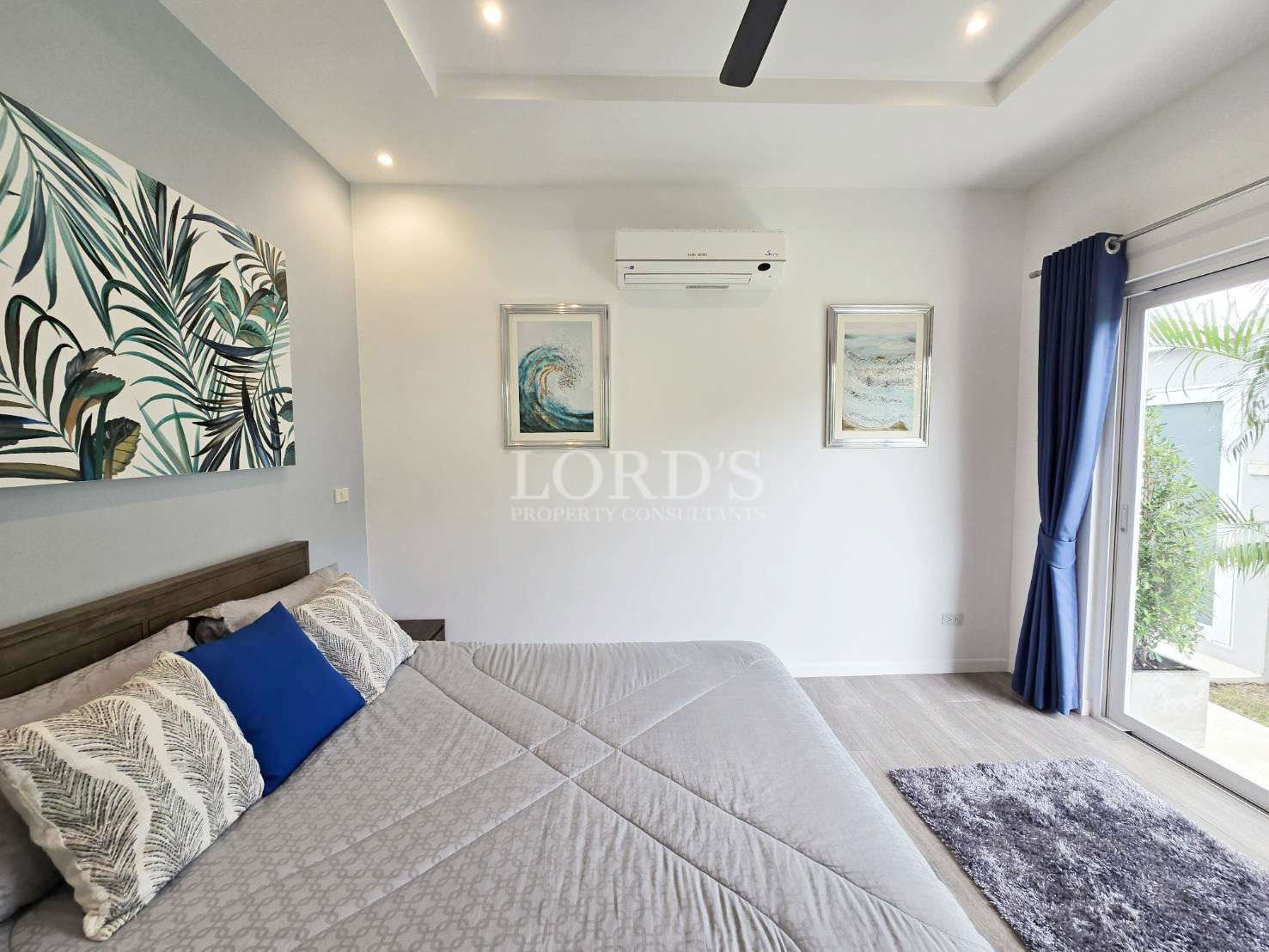 Modern bedroom interior with double bed, wall art, air conditioner, and sliding glass door with blue curtains