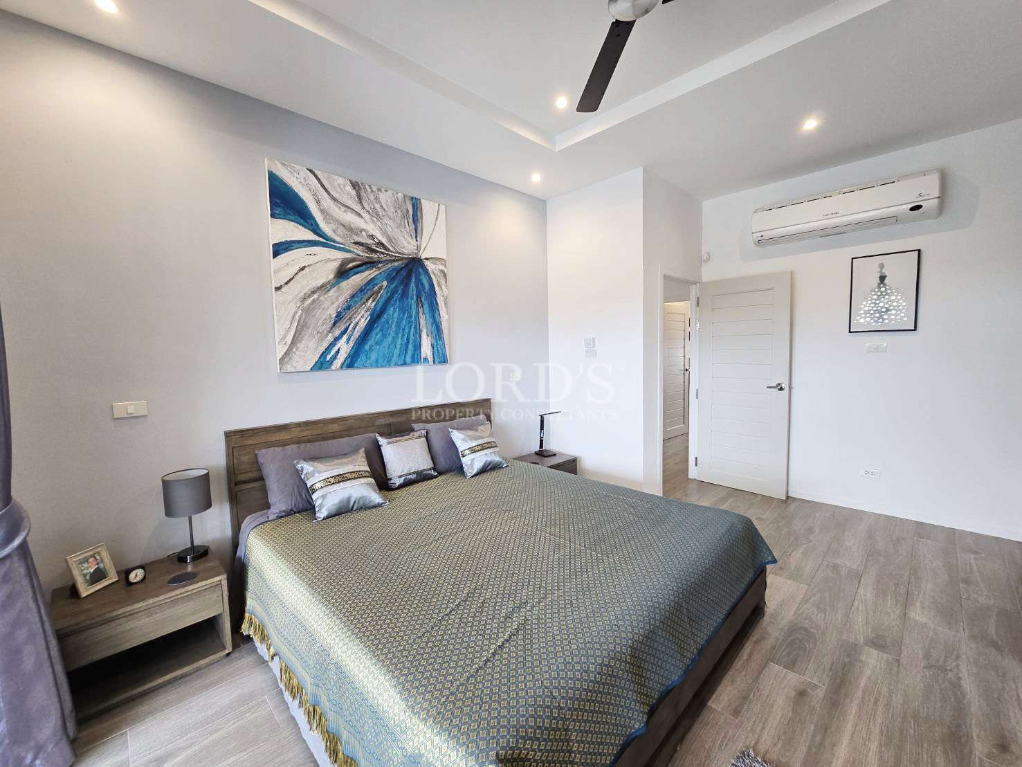 Modern bedroom with double bed, abstract blue wall art, ceiling fan, and air conditioning.