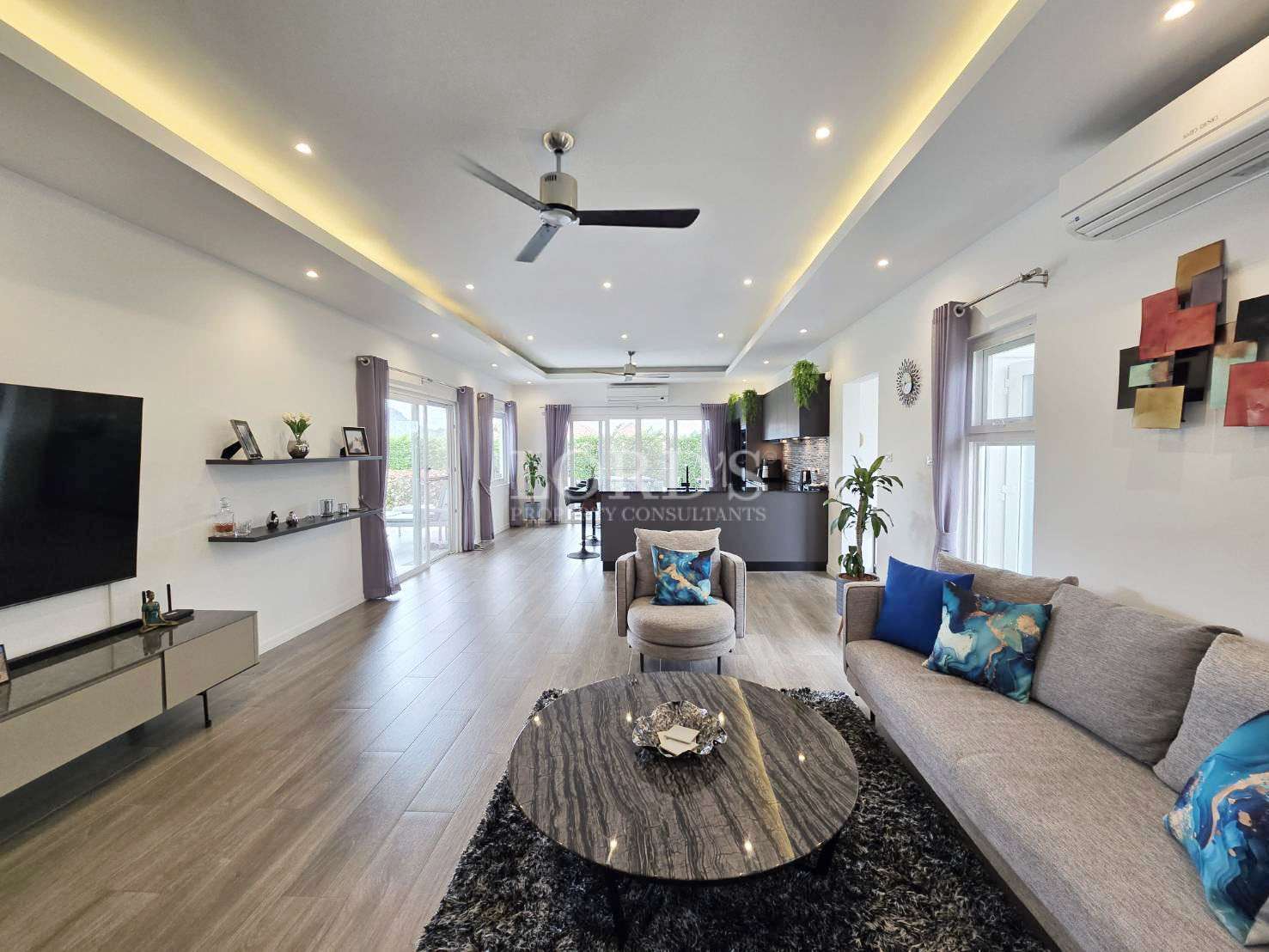 Spacious modern living room with open-plan kitchen, ceiling fan, and large windows.