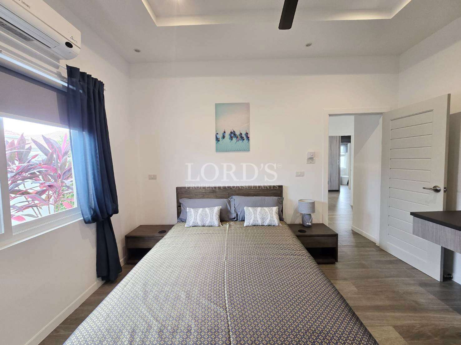 Modern bedroom with double bed, wooden bedside tables, air conditioning, and natural light.