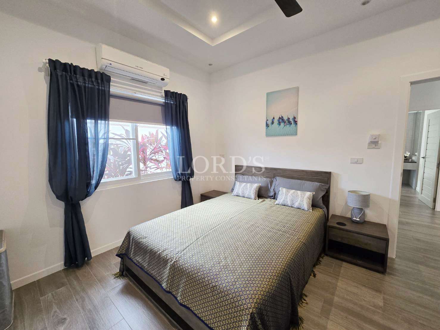 Modern bedroom with double bed, bedside tables, window curtains, and air conditioning.