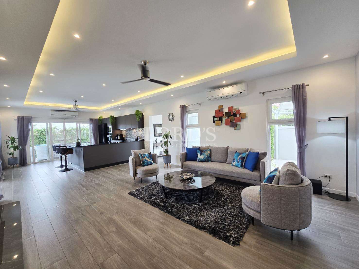 Spacious open-plan living room with modern sofa seating, ceiling lights, and connected kitchen area.