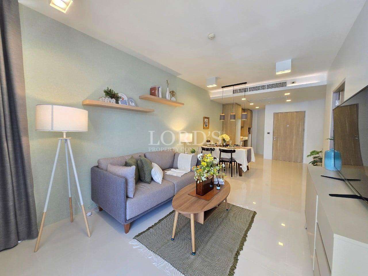 Modern living room with sofa, wooden coffee table, soft lighting, and open dining area in a contemporary apartment.