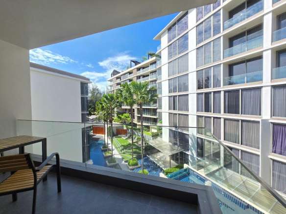 Balcony view of a modern apartment complex with swimming pool, palm trees, and glass railings.