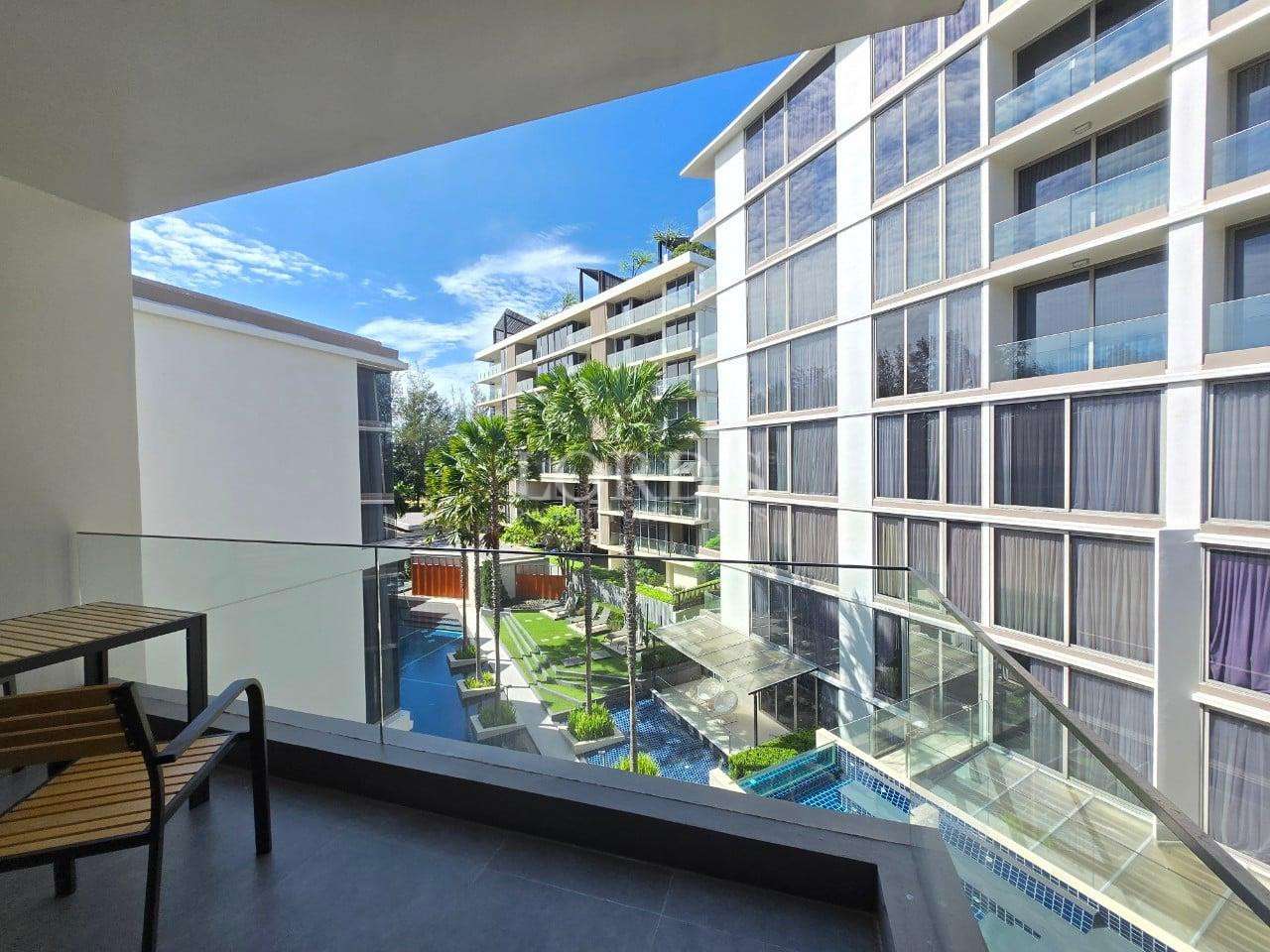 Balcony view of a modern apartment complex with swimming pool, palm trees, and glass railings.
