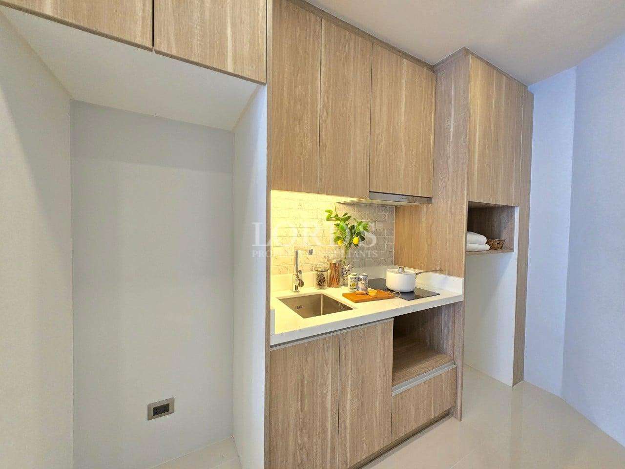 Compact modern kitchenette with wooden cabinets, sink, stovetop, and under-cabinet lighting.