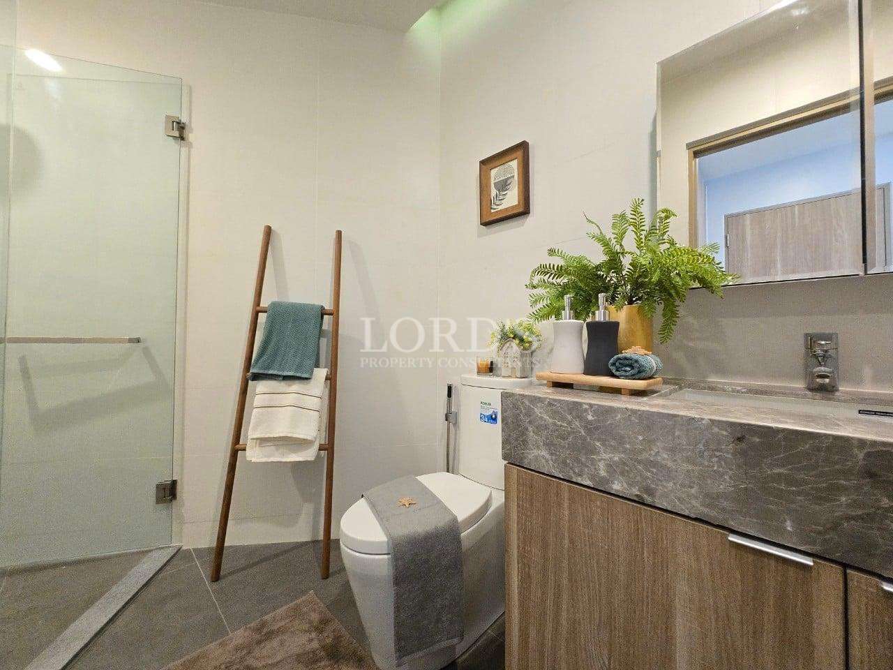 Modern bathroom with glass shower, vanity sink, wooden cabinet, toilet, and indoor plants.