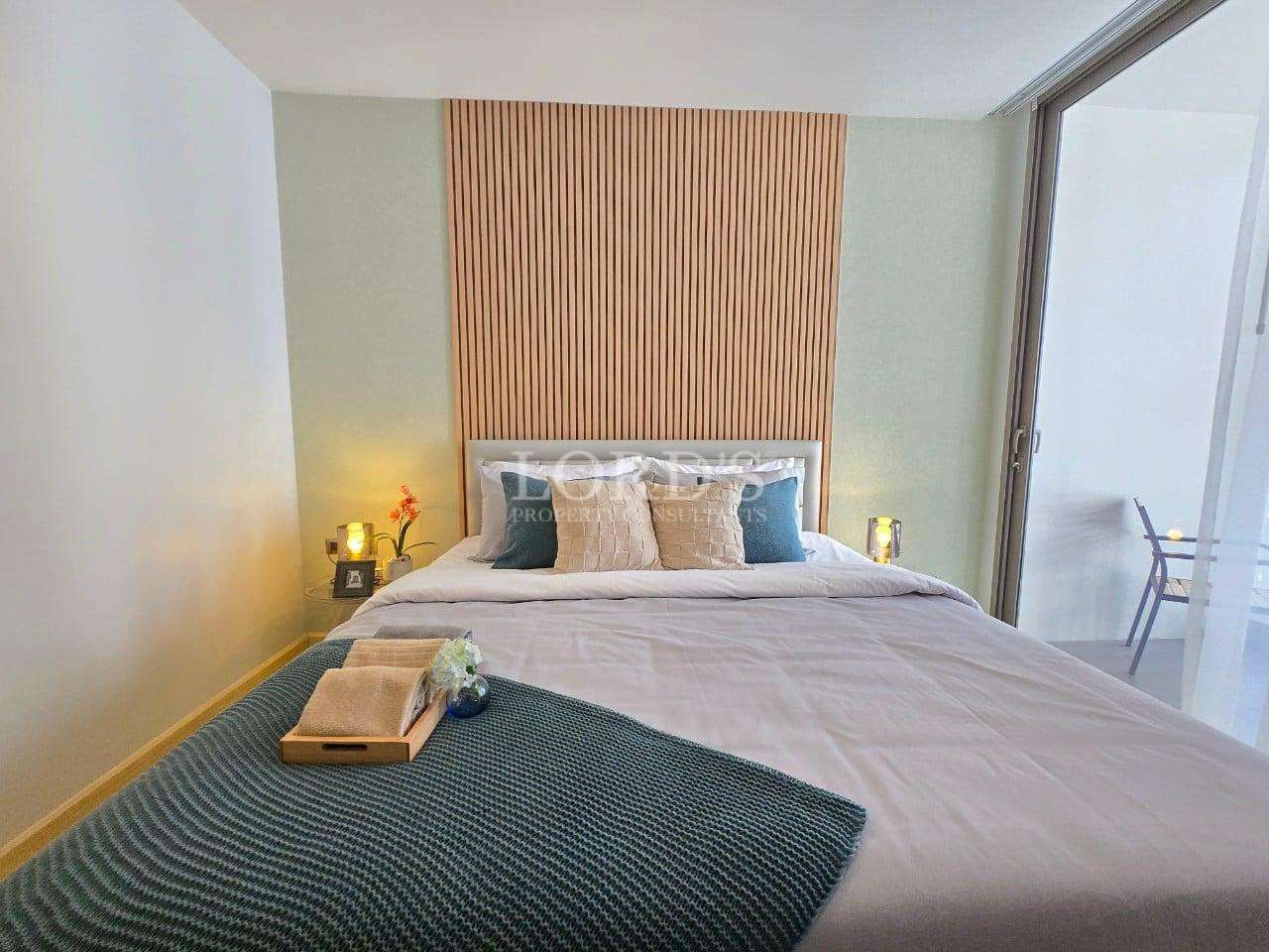 Modern bedroom with double bed, wooden accent wall, soft lighting, and balcony access.