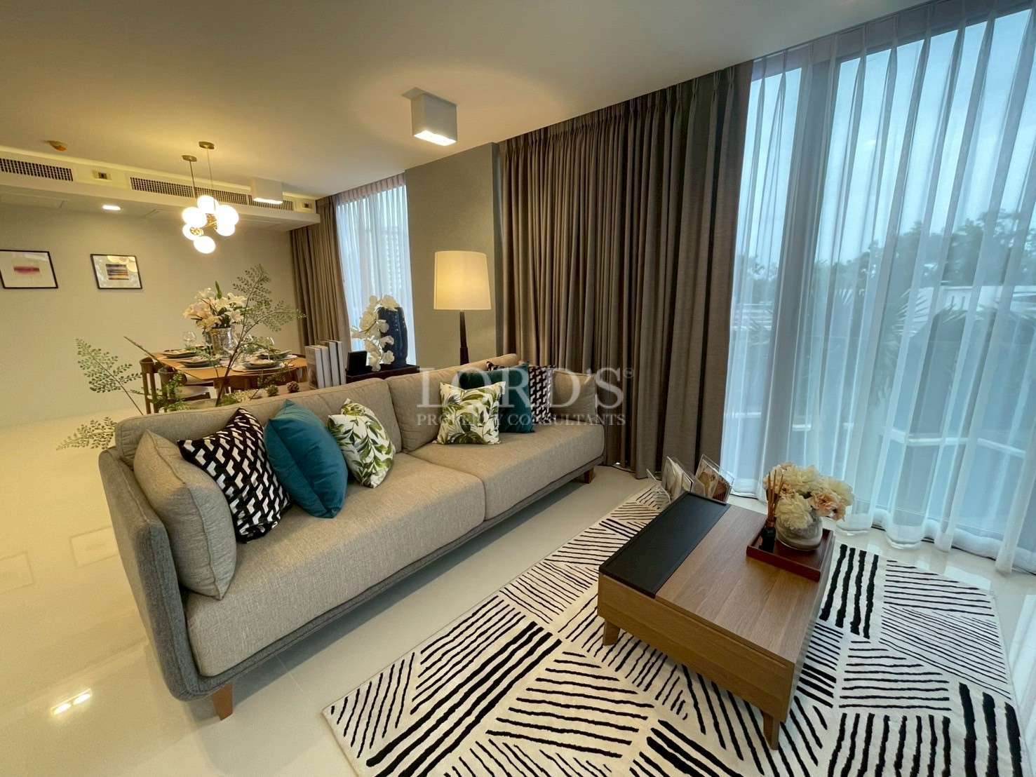 Modern living room with gray sofa, coffee table, patterned rug, and large window curtains.