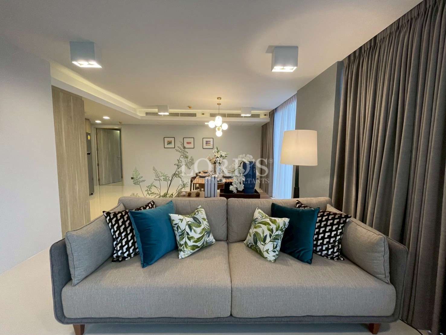 Modern living room with gray sofa, decorative cushions, floor lamp, and open-plan dining area.