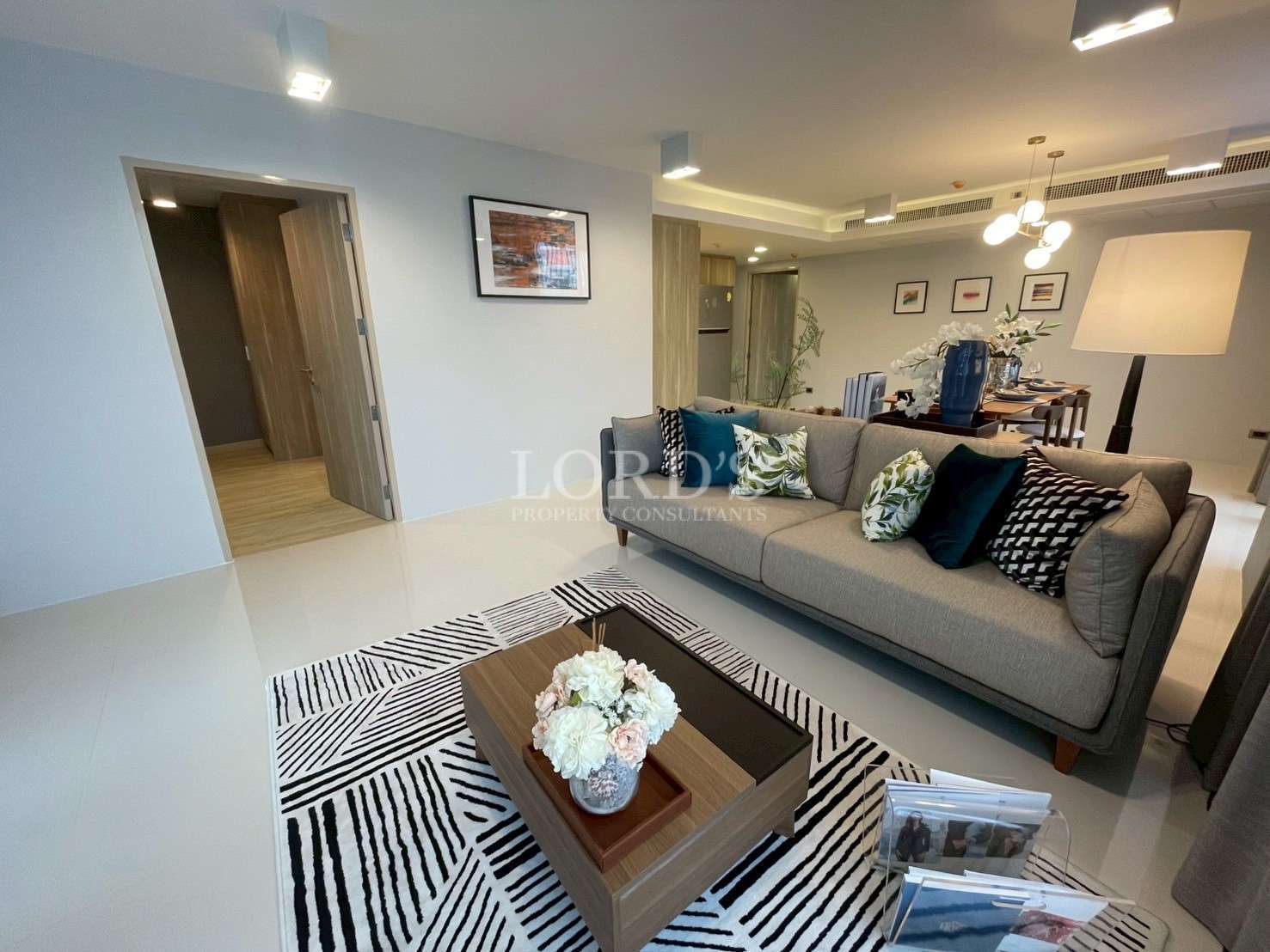 Modern living room with gray sofa, coffee table, patterned rug, and open-plan dining area.