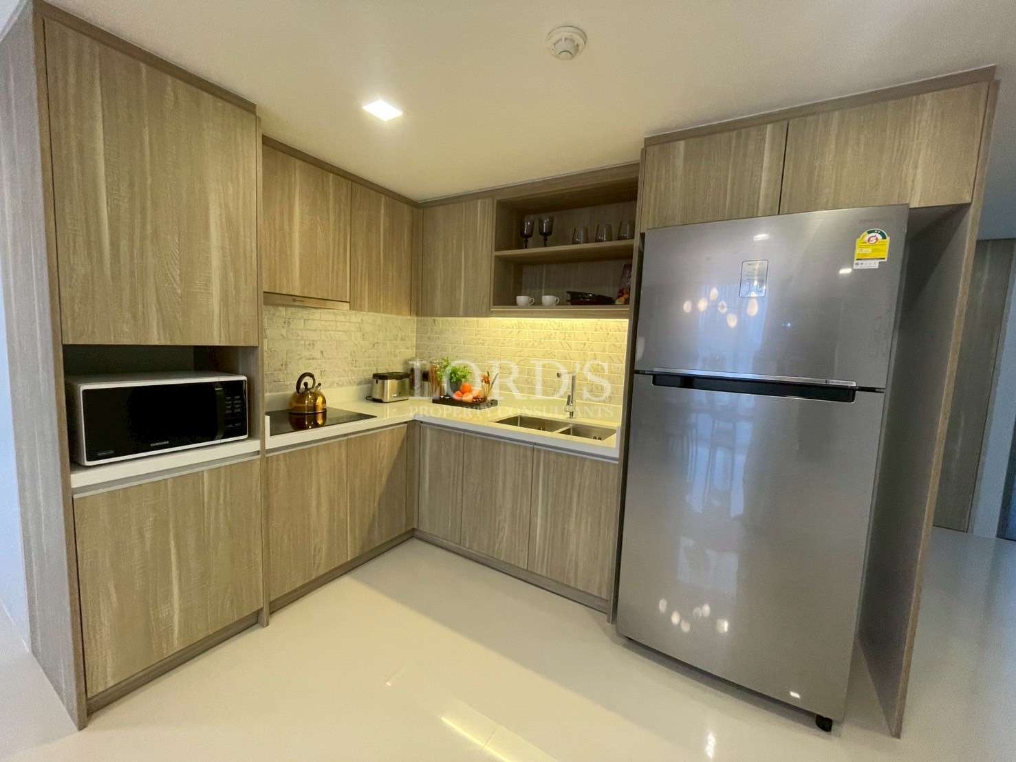 Modern L-shaped kitchen with wooden cabinets, refrigerator, microwave, and built-in sink.