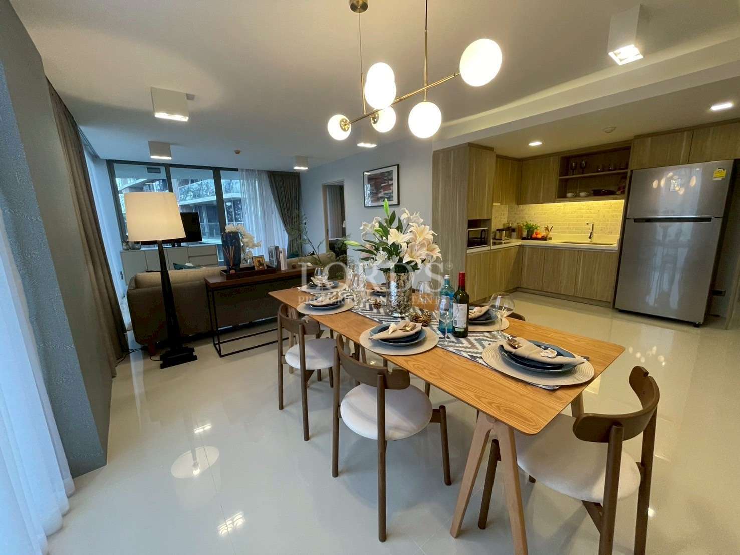 Modern dining and kitchen area with wooden dining table, pendant lights, and open-plan living space.